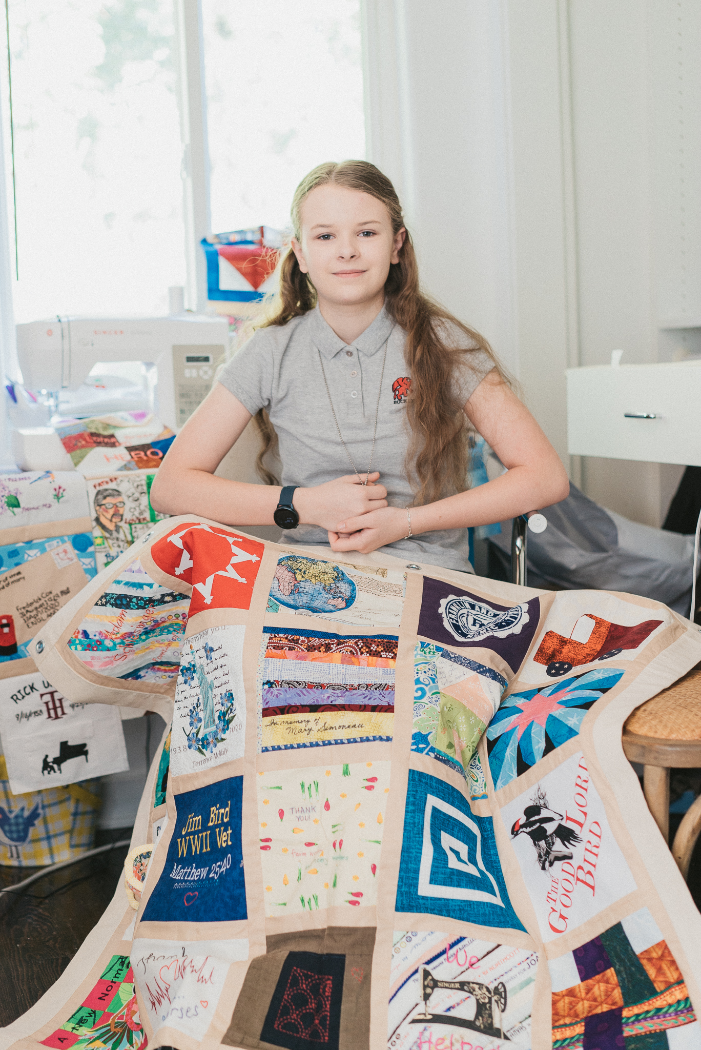 Eighth grader Madeleine Fugate sits in a chair with a panel from the COVID-19 memorial quilt draped over her lap 