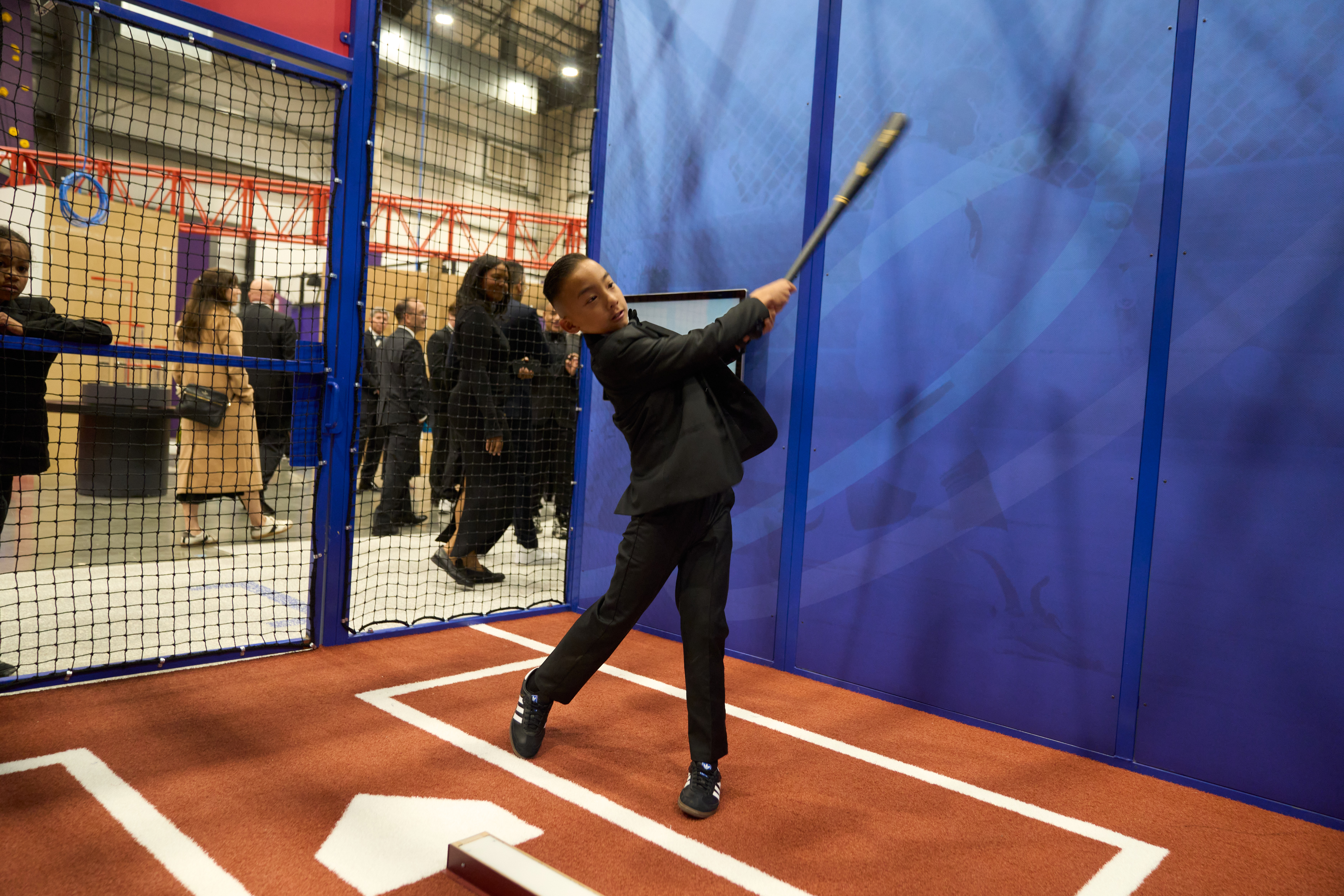 A young guest dressed up in a suit for the 26th Annual Discovery Ball, which featured a preview of the new GAME ON exhibition, is at home plate in the baseball interactive and swings at the ball.