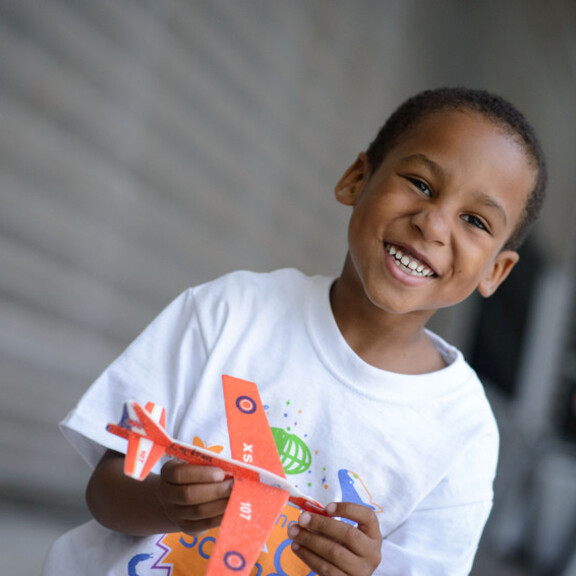 A smiling boy holds a foam plane for a Hands-On Science Camp class