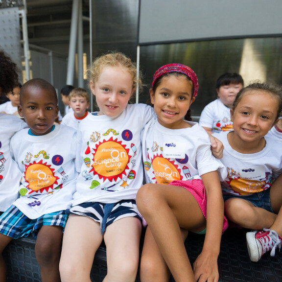 Young kids wearing Hands-On Science Camp shirts sitting in row posing for photo