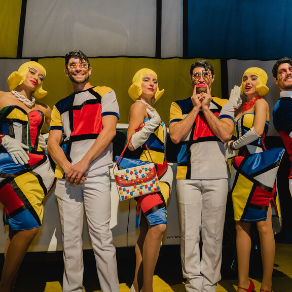 Three female and 3 male entertainers wearing Mondrian inspired costumes  and LEGO minifigure inspired wigs pose in front of Lexus and Mondrian print backdrop