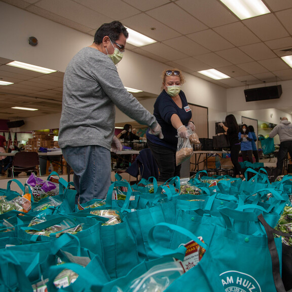 Volunteers wearing masks pack up teal reusable grocery bags with food to be distributed to families in need