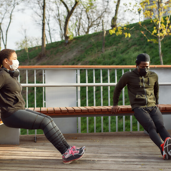 An African-American man and woman exercise outdoors while wearing face masks and staying six feet apart