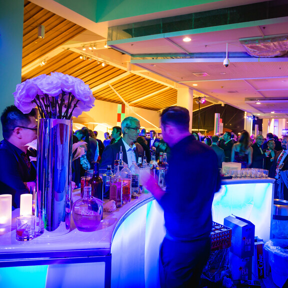 Guests order drinks at blue LED bar on Disney Science Court during a holiday cocktail reception