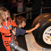 A girl in an astronaut costume with a boy touching space shuttle tires
