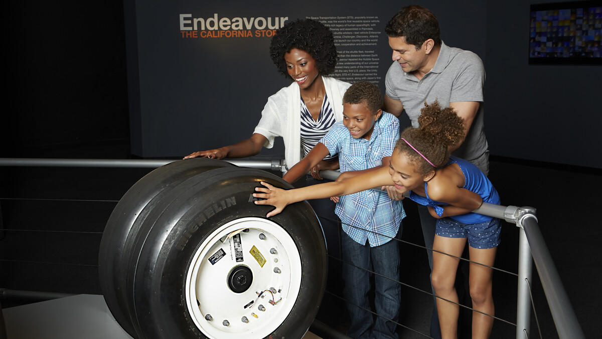 A diverse family touches space shuttle tires in an Endeavour exhibit.