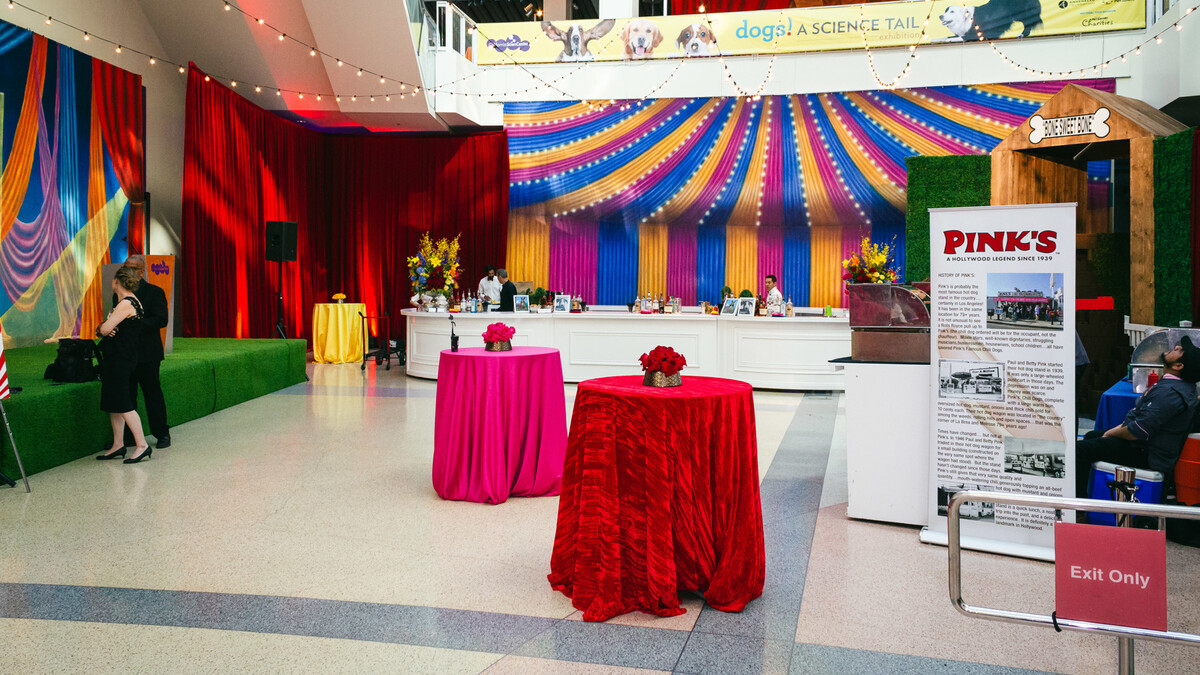 Edgerton Court carnival, circus, themed cocktail reception set up with bright red, pink, and yellow cocktail tables and stage covered in astroturf