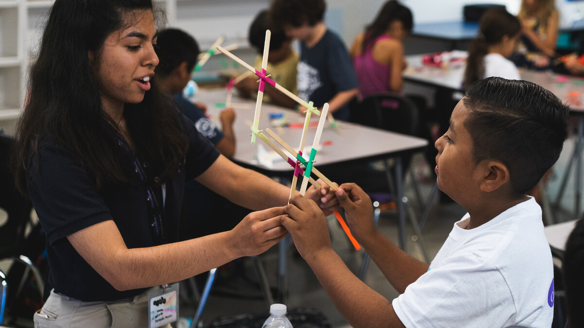 California Science Center educator assists young boy with his wooden stick sculpture