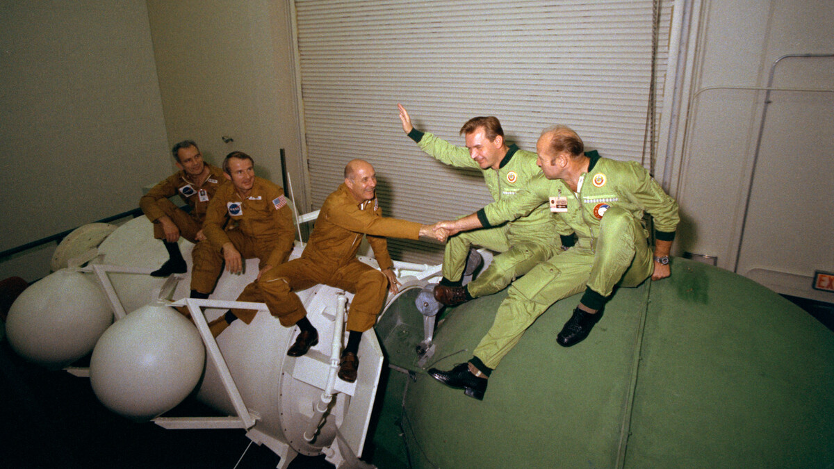 Apollo-Soyuz crew sitting on mockup of their spacecraft while taking a break from training