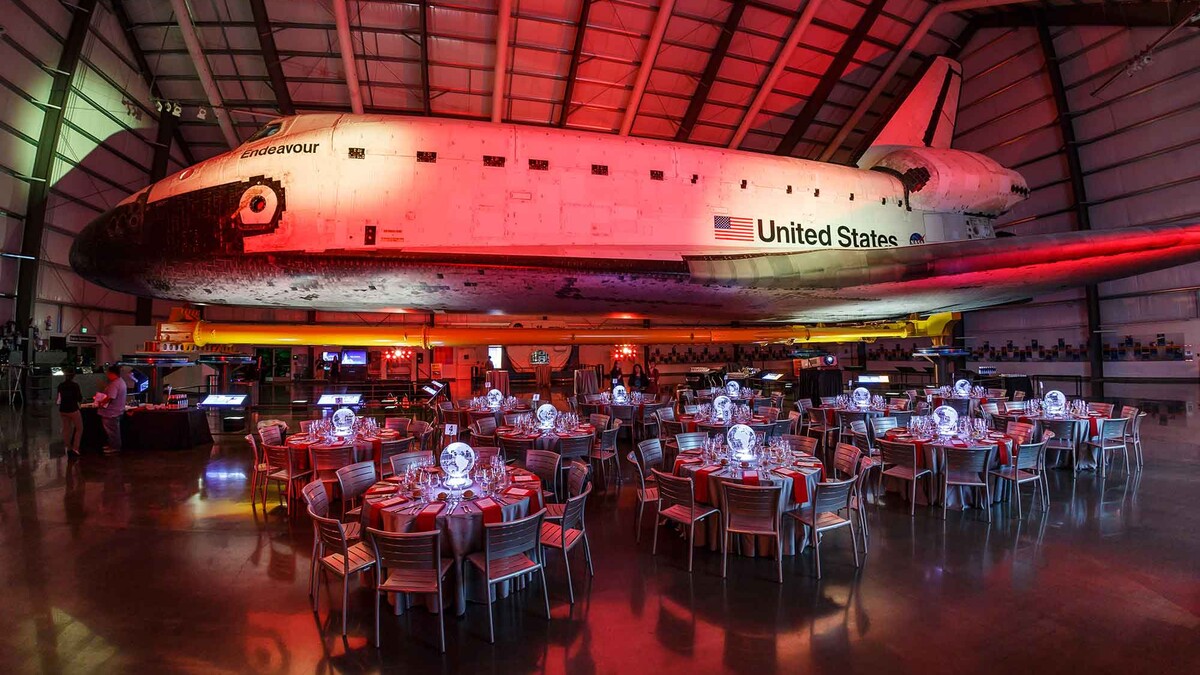 Side view of the Space Shuttle Endeavour lit in red in the Samuel Oschin Pavilion with red banquet tables underneath