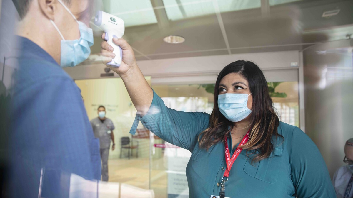 Rocio Trujillo Balderas, volunteer patient screener at Cedars-Sinai, points a temperature scanner at a patient's head