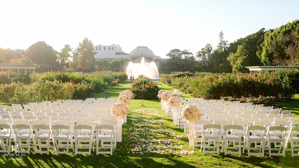 White folding chairs with pink floral accents set in Exposition Park Rose Garden for wedding ceremony