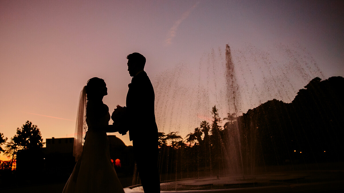 A bride and groom stand silhouetted against the Rose Garden fountain at sunset