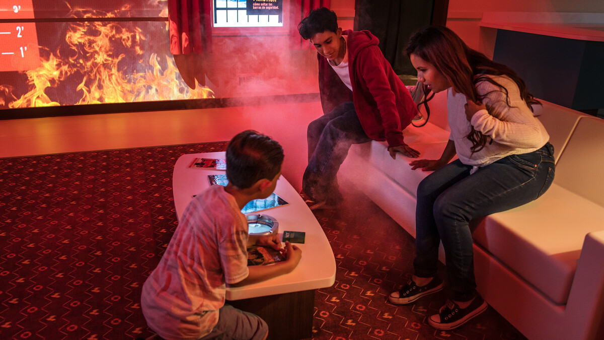 A family sits around a coffee table with a realistic-looking fire on the wall near them.
