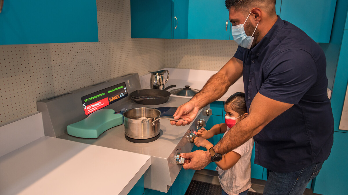 A dad and daughter work together at an interactive kitchen stove exhibit.