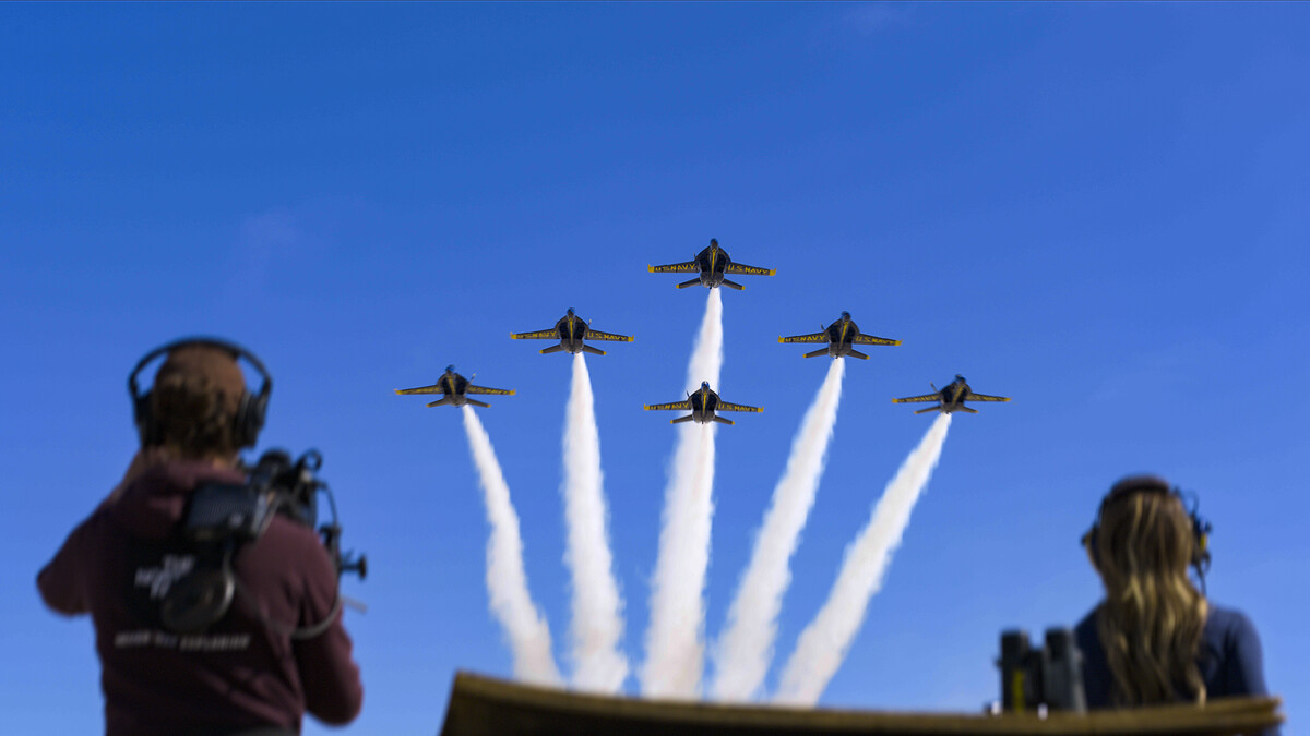 Blue Angels fly in formation against a deep blue sky, as people watch from below.