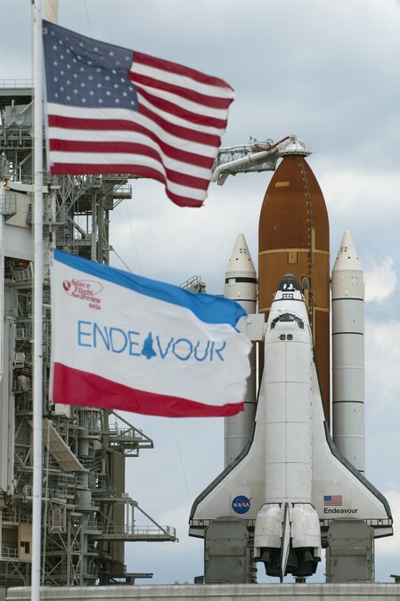 Space Shuttle Endeavour on the launch pad, with the American flag and an Endeavour flag in the foreground