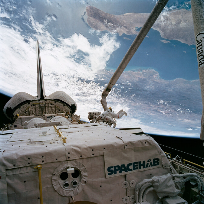 A SPACEHAB module is visible in the payload bay as Endeavour orbits Earth.