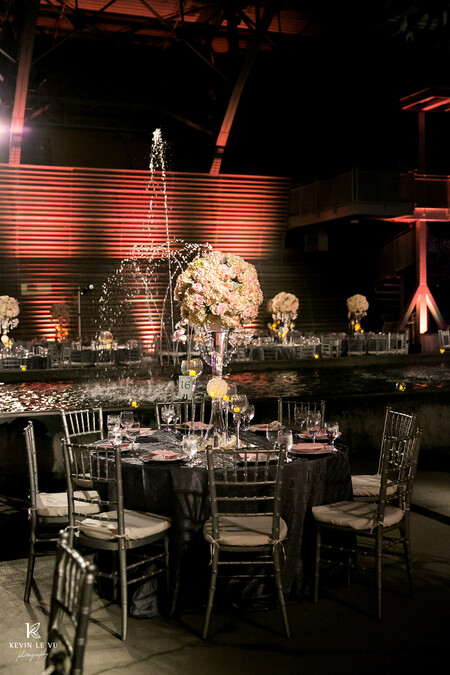 Silver Chiavari chairs sit at a table dressed in dark grey linen with a tall white and pink bouquet on top. 
